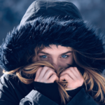 نمای نزدیک از دختری که در فصل زمستان کاپشن پوشیده و با دو دست خود جلوی صورتش را گرفته است.