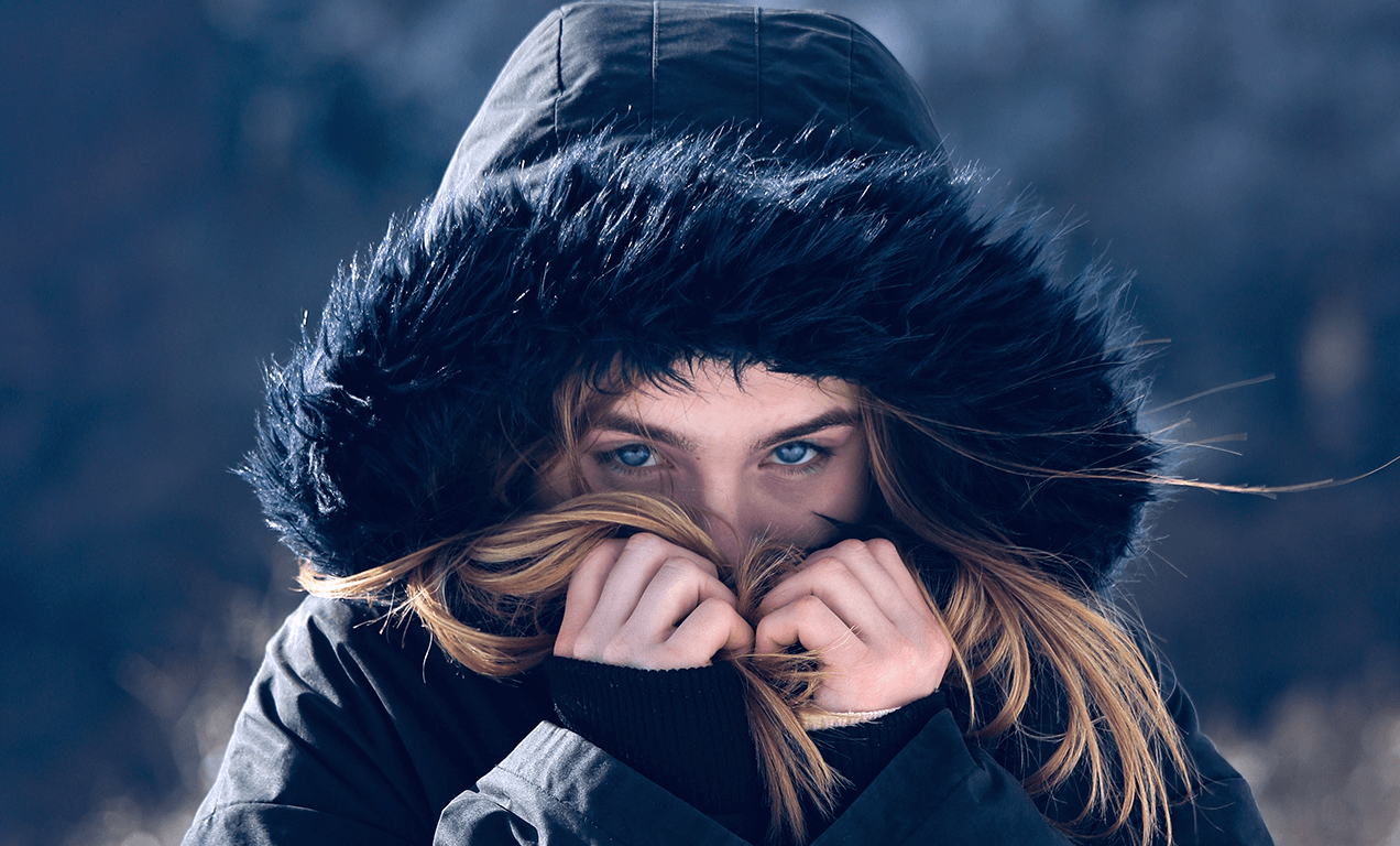 نمای نزدیک از دختری که در فصل زمستان کاپشن پوشیده و با دو دست خود جلوی صورتش را گرفته است.