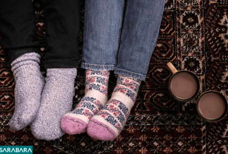 عکس از نمای بالا از زوجی که جوراب پشمی پوشیده اند و دو لیوان در کنارشان است.
