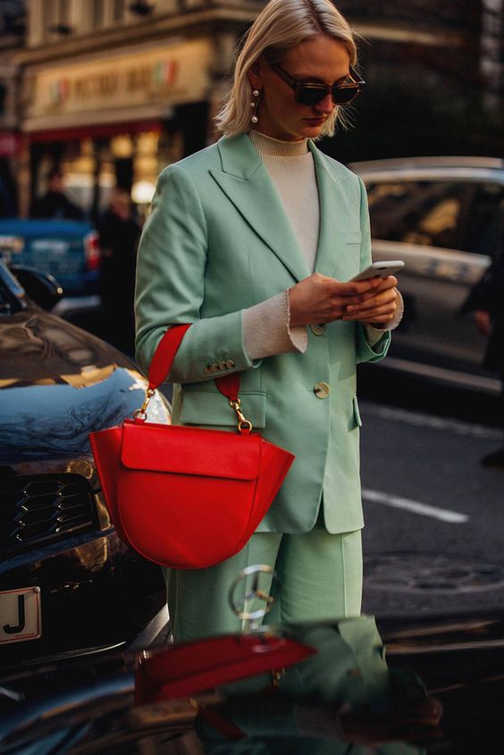 کت و شلوار سبز پاستلی زن با موهای روشن عینک دودی و کیف قرمز